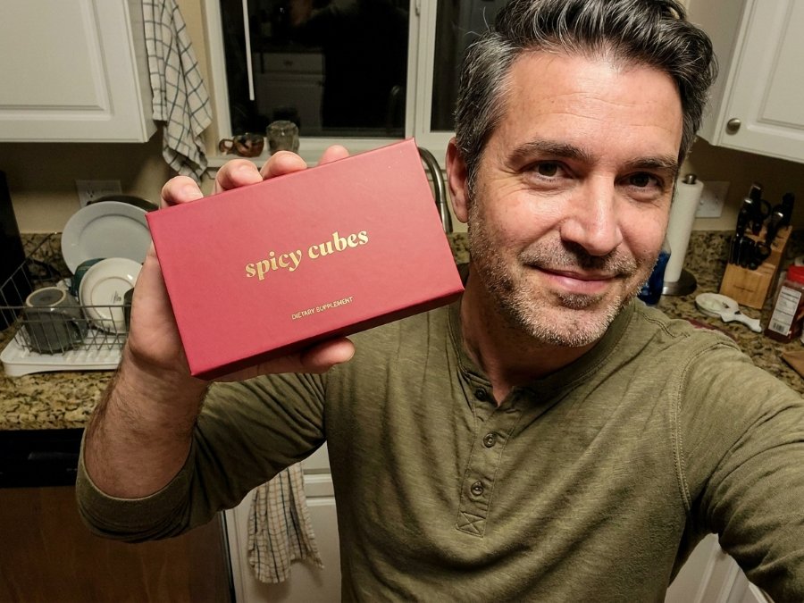 A man in his kitchen holding up the red Spicy Cubes box